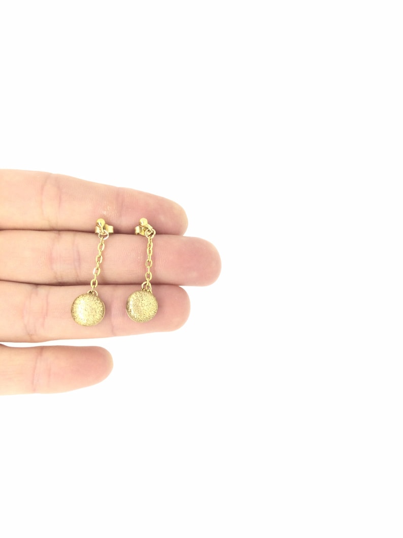 May include: A pair of gold dangle earrings with small round discs at the end of the chains.
