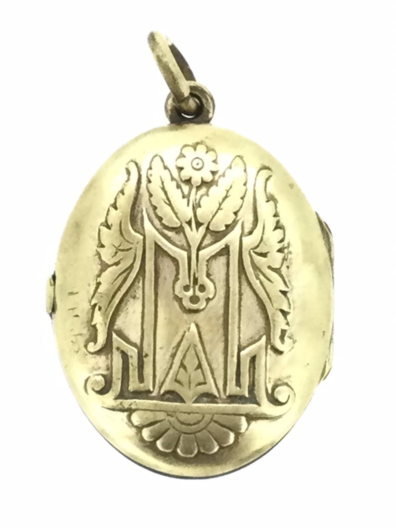 K&ouml;nnte beinhalten: Goldenes ovales Medaillon mit einem gravierten Blumendesign und einem Monogramm. Das Medaillon hat einen Klappdeckel und eine Schlaufe zum Anbringen einer Kette.
