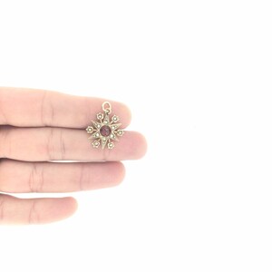 May include: A gold pendant in the shape of a star with a red gemstone in the center and small white gemstones around the edges.