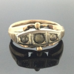Op de afbeelding: Een gouden en zilveren ring met drie ronde stenen gezet in een decoratieve band.
