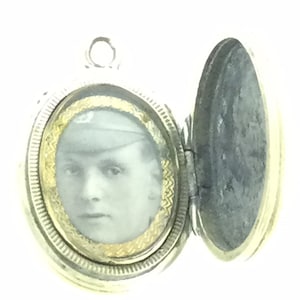May include: Silver oval locket with a hinged lid. The locket has a gold-colored trim and a black and white photo of a man inside.