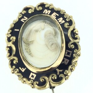 May include: A gold oval locket with black enamel trim and a glass insert containing a lock of hair. The locket has the inscription "IN MEMORY" around the edge.