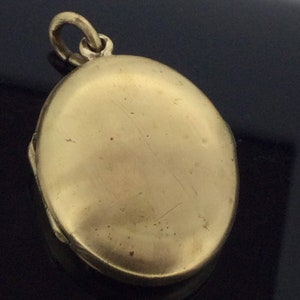 K&ouml;nnte beinhalten: Ein ovales Medaillon in Goldton mit einem Scharnierdeckel und einer Schlaufe zum Anbringen einer Kette. Das Medaillon ist geschlossen und die Oberfl&auml;che ist glatt.