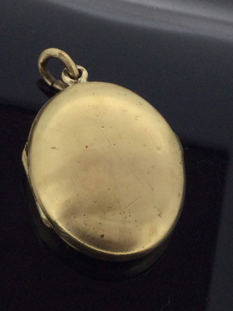 K&ouml;nnte beinhalten: Ein ovales Medaillon in Goldton mit einem Scharnierdeckel und einer Schlaufe zum Anbringen einer Kette. Das Medaillon ist geschlossen und die Oberfl&auml;che ist glatt.