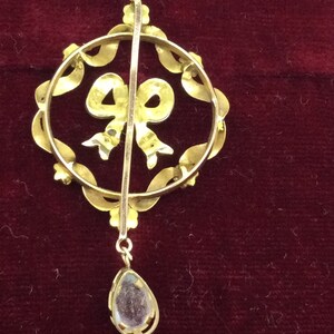 May include: A gold pendant with a clear stone drop and a bow design. The pendant is made of gold and has a delicate design.
