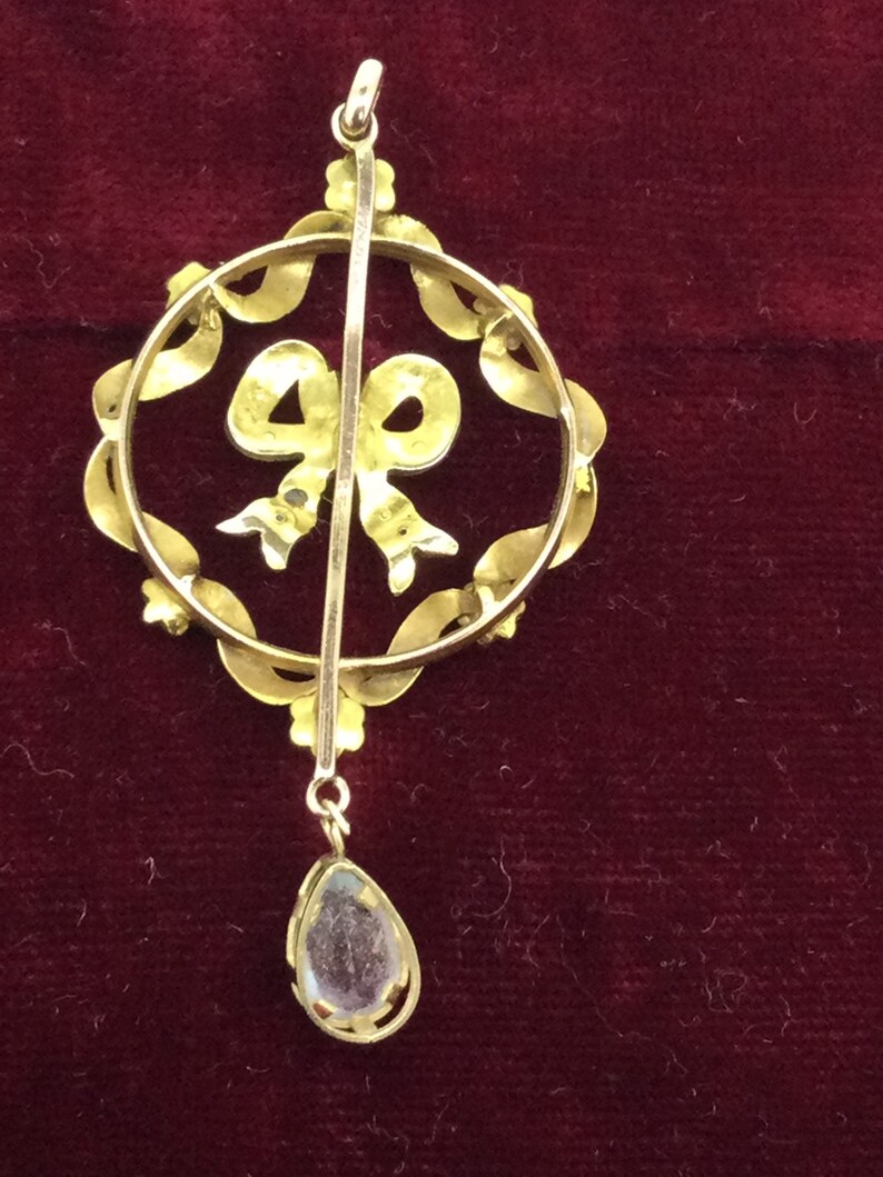 May include: A gold pendant with a clear stone drop and a bow design. The pendant is made of gold and has a delicate design.