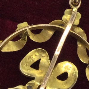 May include: A gold pendant with a bow design and a small, round, blue stone. The back of the pendant has a hallmark that reads "14K".