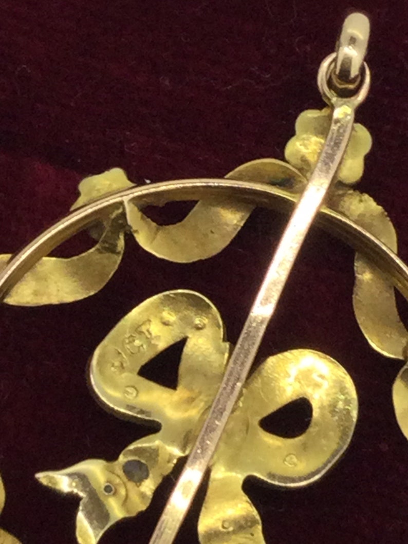 May include: A gold pendant with a bow design and a small, round, blue stone. The back of the pendant has a hallmark that reads "14K".