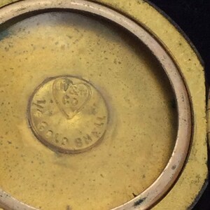 以下が含まれることがあります： ハート型のデザインと「W. GOULD & CO.  SMALL」という刻印が施された、金色の金属製のロケットのクローズアップ。