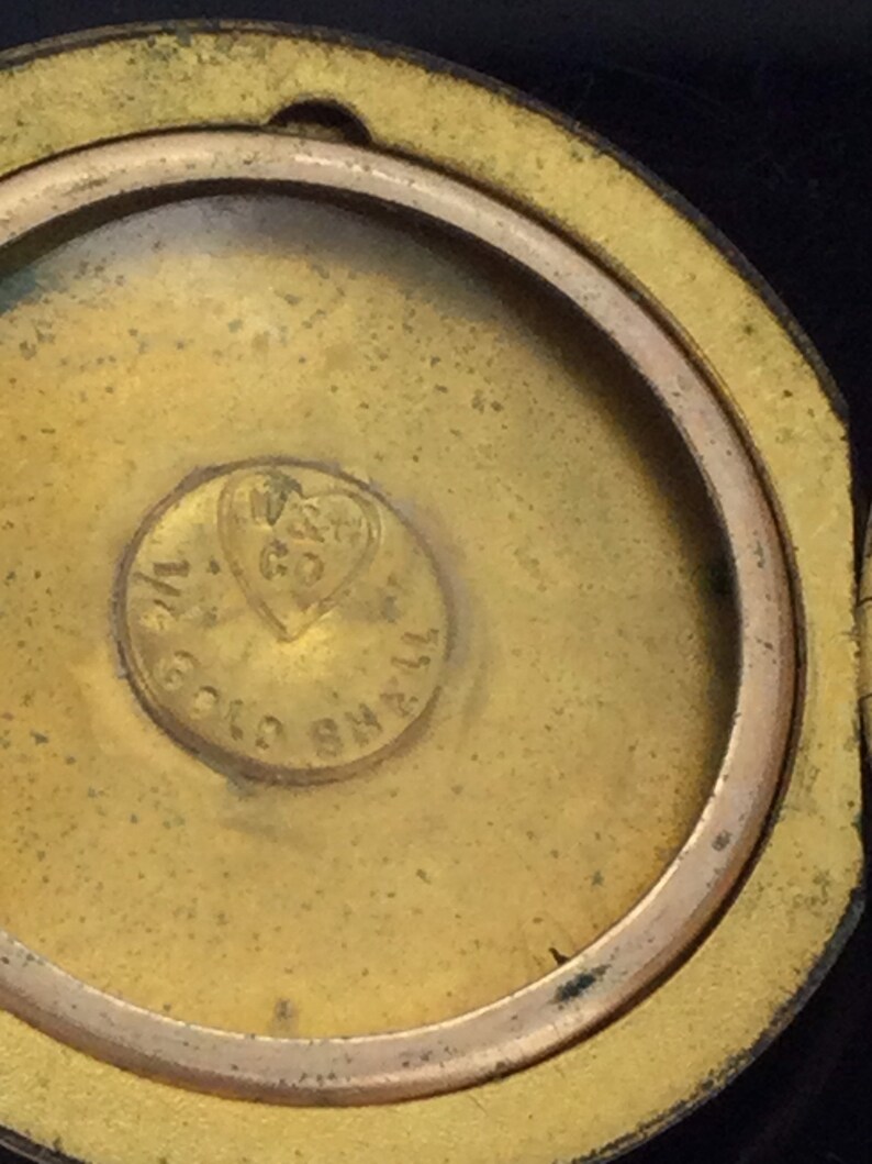 以下が含まれることがあります： ハート型のデザインと「W. GOULD & CO.  SMALL」という刻印が施された、金色の金属製のロケットのクローズアップ。