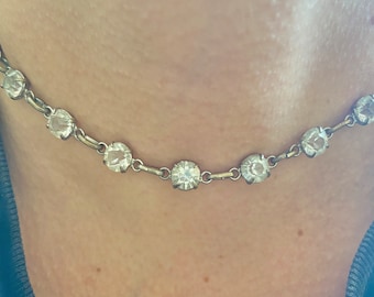 May include: A silver chain necklace with clear round rhinestones. The necklace is delicate and has a simple design.