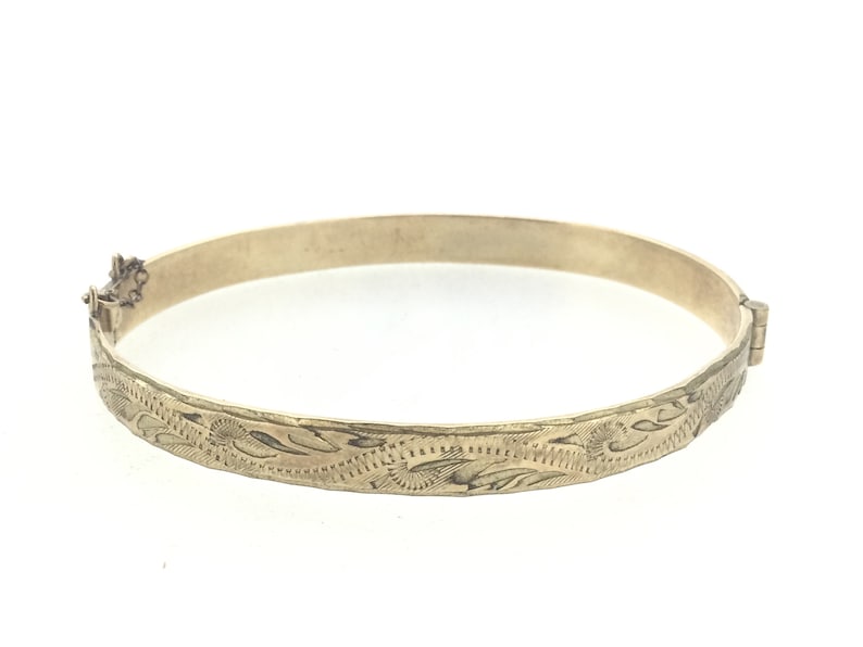K&ouml;nnte beinhalten: Ein goldenes Armreif-Armband mit einem floralen, gravierten Design.
