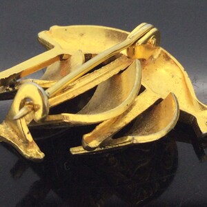 May include: Gold-toned metal brooch with a dolphin design. The brooch has a pin and catch closure on the back.