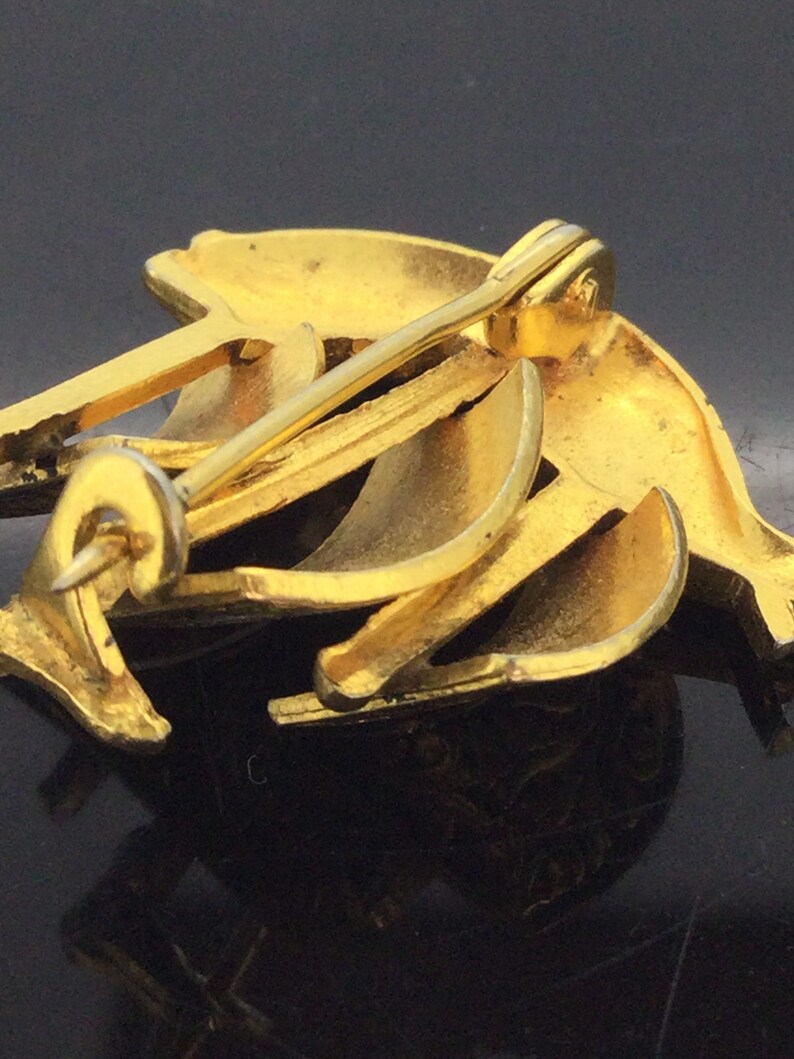 May include: Gold-toned metal brooch with a dolphin design. The brooch has a pin and catch closure on the back.