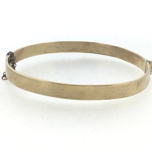 K&ouml;nnte beinhalten: Ein goldenes Armreif-Armband mit einem Scharnierverschluss. Das Armband ist schlicht und hat keine Verzierungen.