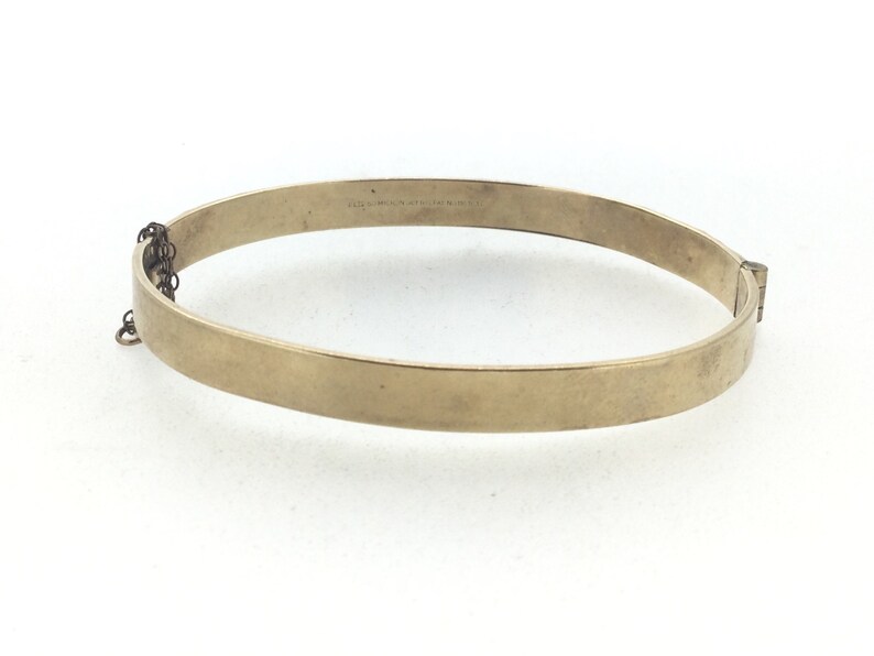 K&ouml;nnte beinhalten: Ein goldenes Armreif-Armband mit einem Scharnierverschluss. Das Armband ist schlicht und hat keine Verzierungen.