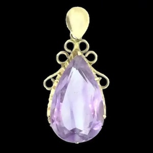May include: A gold pendant featuring a large, faceted amethyst gemstone in a pear shape. The pendant has a delicate, ornate design with intricate swirls.