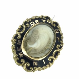 May include: A gold-toned oval locket with black enamel and a white hair cameo. The locket has the words "MEMORY" and "FOR EVER" inscribed around the edge.