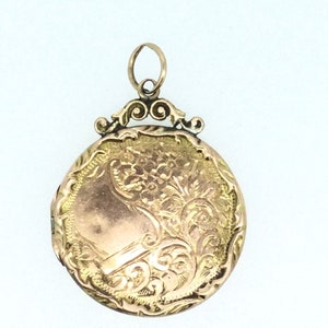 May include: A gold locket with an ornate floral design. The locket has a hinged lid and a loop for attaching a chain.