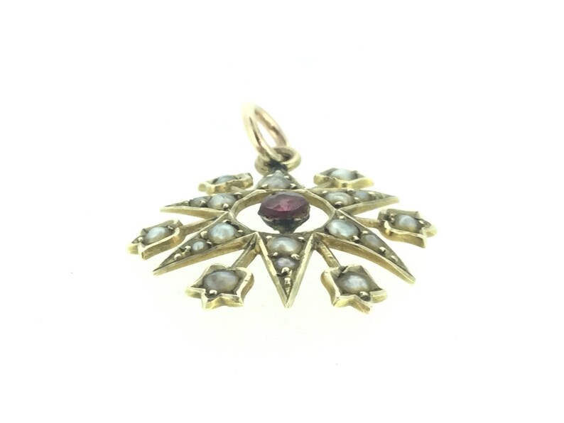 May include: A gold pendant with a red gemstone in the center surrounded by a circle of pearls. The pendant is shaped like a star with eight points.