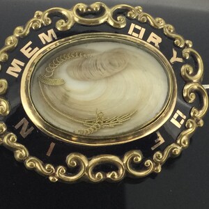 May include: Gold-toned oval locket with black enamel and gold lettering that reads "MEMORY" and "DEARLY". The locket contains a lock of hair.