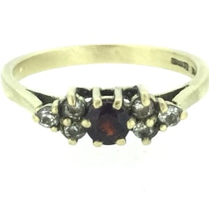 Puede incluir: Un anillo de oro con una piedra roja rodeada de piedras pequeñas transparentes.