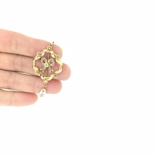 May include: A gold pendant with a pearl bow design and a teardrop-shaped crystal hanging from the bottom.