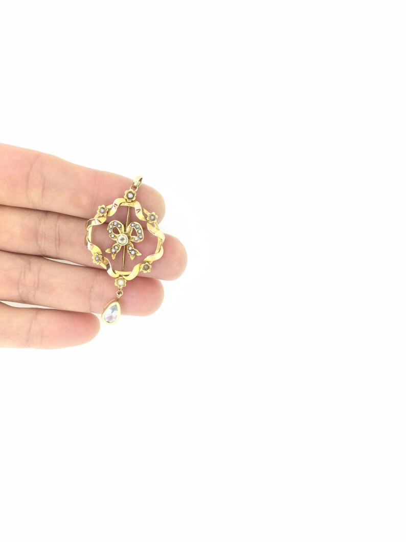 May include: A gold pendant with a pearl bow design and a teardrop-shaped crystal hanging from the bottom.