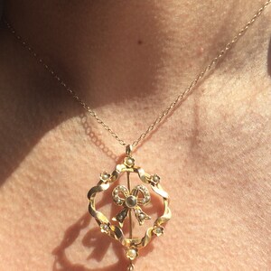 May include: A gold necklace with a pendant featuring a pearl-encrusted bow and a teardrop-shaped gemstone.
