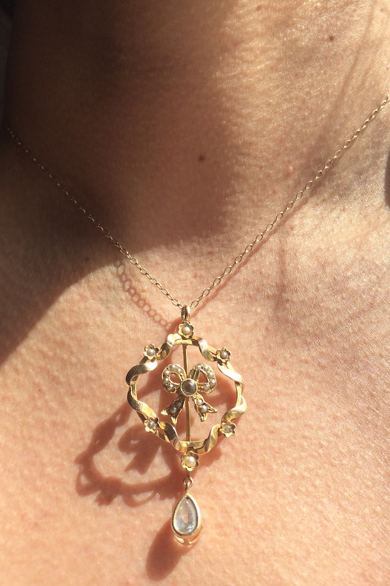 May include: A gold necklace with a pendant featuring a pearl-encrusted bow and a teardrop-shaped gemstone.