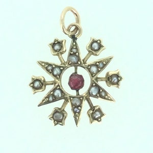 May include: A gold pendant with a red gemstone in the center, surrounded by a starburst design with small white pearls.