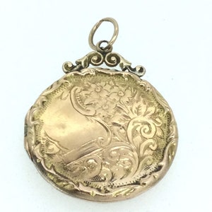 May include: A gold locket with an ornate floral design. The locket has a hinged lid and a loop for attaching a chain.