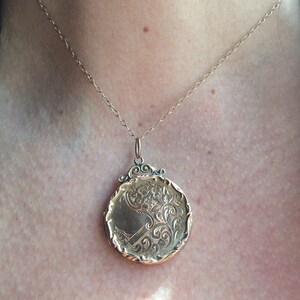 May include: A gold locket necklace with a detailed floral design. The locket is round and has a delicate chain.