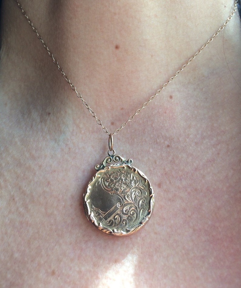 May include: A gold locket necklace with a detailed floral design. The locket is round and has a delicate chain.