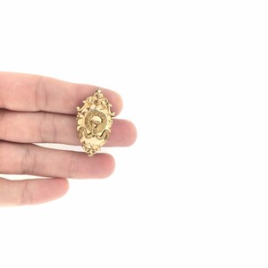 May include: A gold-toned pendant with an ornate design featuring a letter 'Q' in the center.