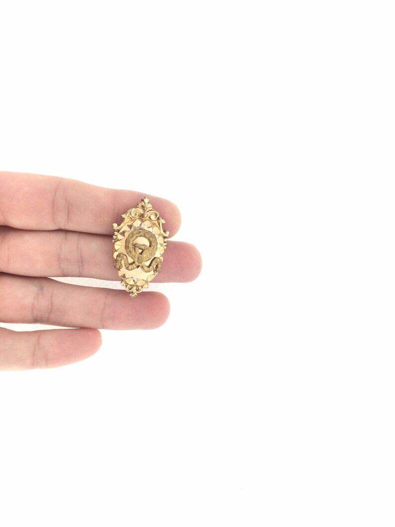 May include: A gold-toned pendant with an ornate design featuring a letter 'Q' in the center.