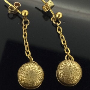 May include: A pair of gold dangle earrings with a delicate chain and a round, textured charm. The charms have a floral design.