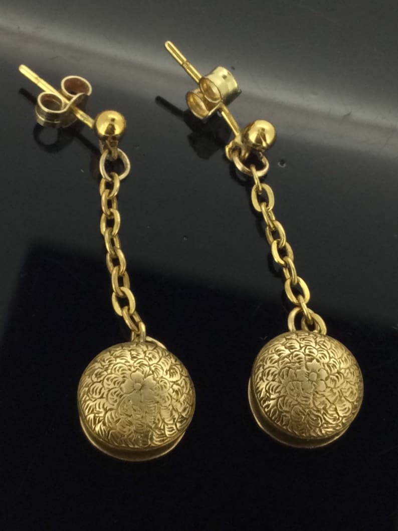 May include: A pair of gold dangle earrings with a delicate chain and a round, textured charm. The charms have a floral design.