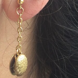 May include: Gold chain earrings with two round charms. The charms have an intricate, floral design.