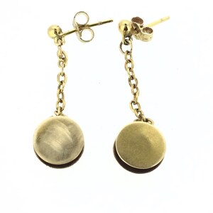 May include: A pair of gold drop earrings with a round disc pendant hanging from a chain. The earrings have a simple, elegant design.