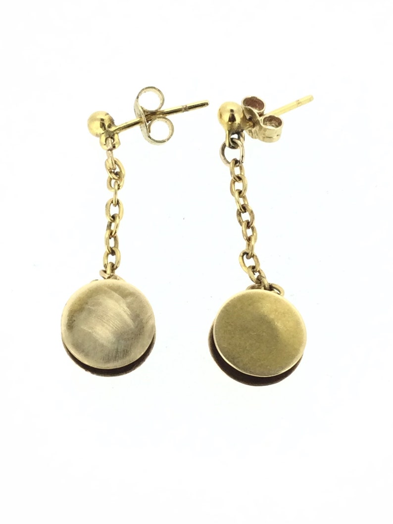 May include: A pair of gold drop earrings with a round disc pendant hanging from a chain. The earrings have a simple, elegant design.