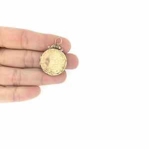 May include: A gold locket pendant with an ornate design. The locket is closed and has a loop for attaching a chain.