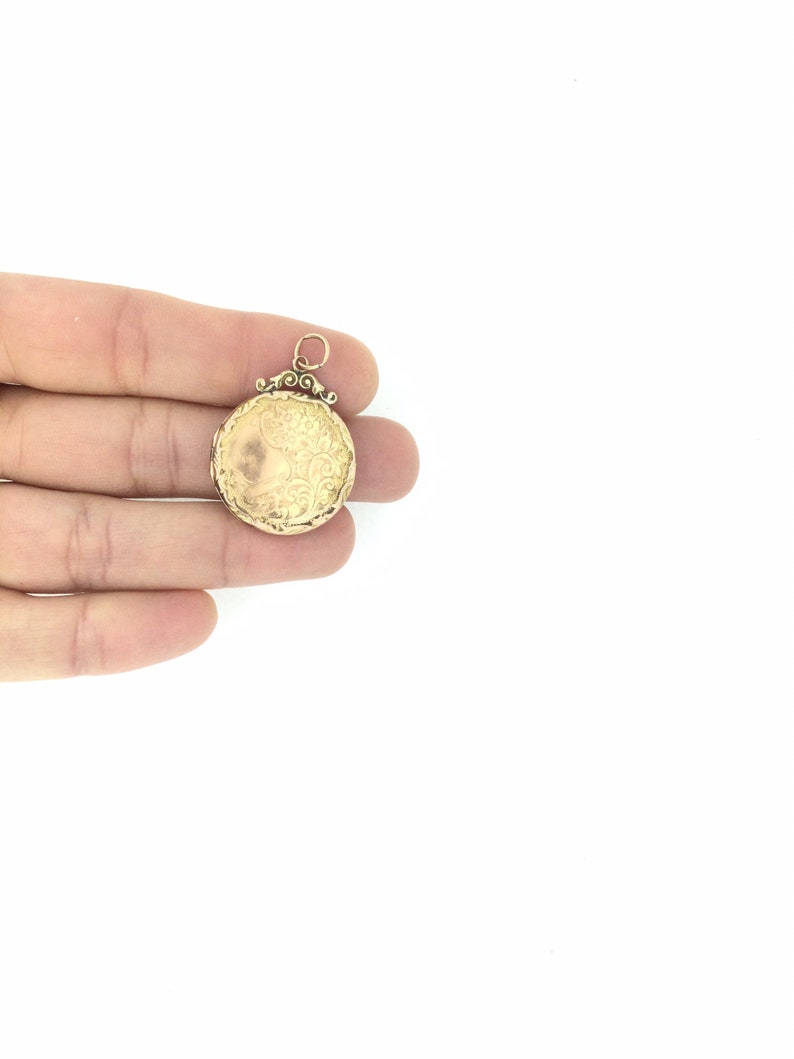 May include: A gold locket pendant with an ornate design. The locket is closed and has a loop for attaching a chain.