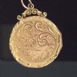 May include: A gold locket with an ornate, engraved design. The locket has a loop at the top for attaching a chain.