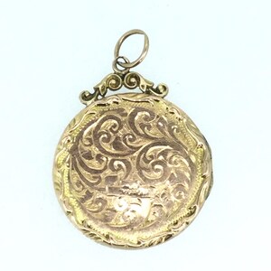 May include: A gold locket with an ornate, engraved design. The locket has a round shape and a bail with a decorative loop.