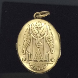 K&ouml;nnte beinhalten: Ein ovales goldenes Medaillon mit einem gravierten floralen Design und dem Buchstaben "M".