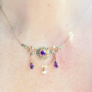 May include: A gold necklace with a delicate design featuring a central amethyst stone surrounded by pearls. The necklace has three dangling drops, each with a pear-shaped amethyst and a pearl.