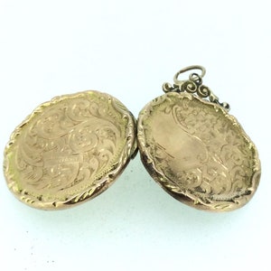 May include: A gold locket with an intricate engraved design. The locket is open, revealing the inside of the locket. The locket has a loop for a chain.