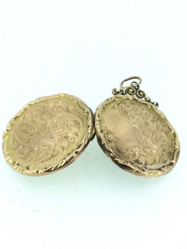 May include: A gold locket with an intricate engraved design. The locket is open, revealing the inside of the locket. The locket has a loop for a chain.