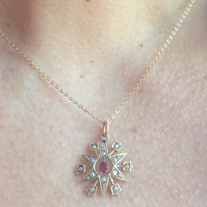 May include: A gold necklace with a star-shaped pendant. The pendant is decorated with small white pearls and a red gemstone in the center.